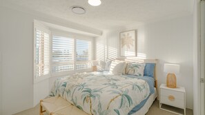 A bedroom with a bed, a nightstand, a bench, a window with blinds, and a ceiling light.