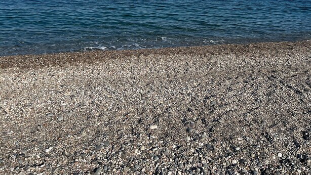 Ein Kiesstrand mit freiem Blick auf das Meer und einen klaren Himmel.