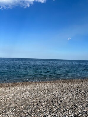 A pebbled beach with a clear view of the sea and a clear sky.
