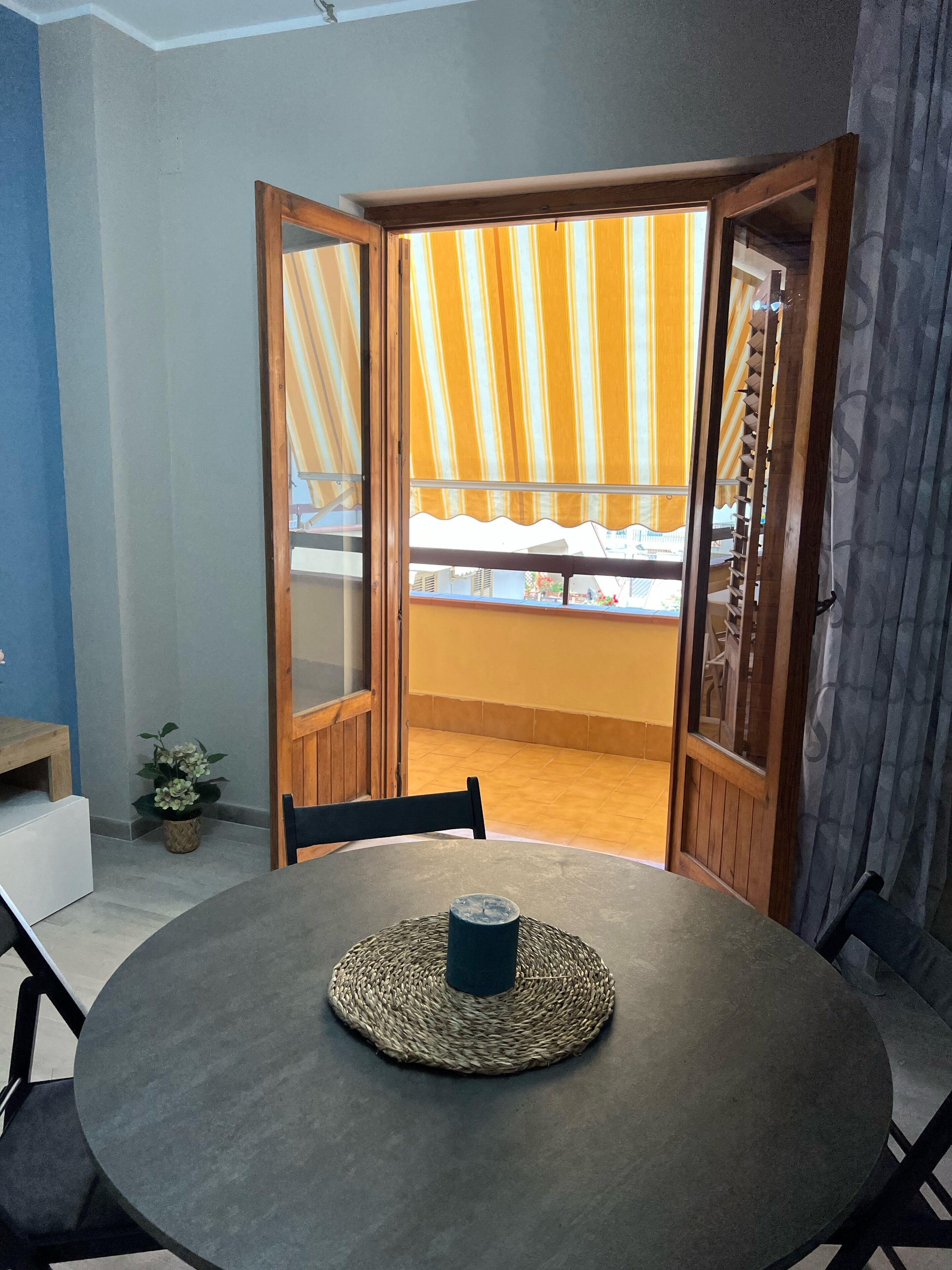 A room with a round table, chairs, and a view through a wooden door with striped curtains.