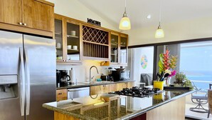 Una cocina moderna con refrigerador de acero inoxidable, armarios de madera, encimera de granito y una isla grande con estufa a gas.