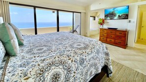 Un dormitorio amplio con una cama grande, un aparador de madera, un televisor de pantalla plana y un balcón con vista al océano.