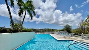 Una piscina rectangular con agua azul cristalina, rodeada por una solana blanca y una escalera de metal.