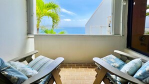 Un balcón con vista al mar, dos sillones de relax y una ventana con persianas.