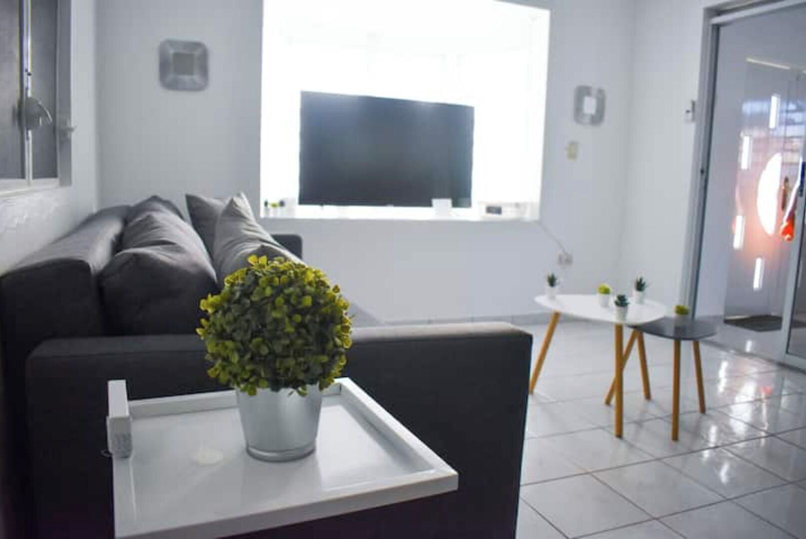 Ein modernes Wohnzimmer mit einer Couch, einem kleinen Tisch mit Topfpflanze und einem Fernseher an der Wand.