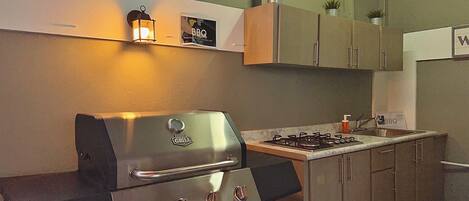 Une cuisine équipée d’un barbecue en acier inoxydable, d’une cuisinière à gaz et de meubles de rangement en bois.