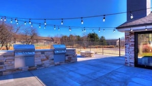 An outdoor patio with stone walls, a barbecue grill, and string lights. - Lovely 2-Bdrm unit with pool. Home away from home. (Naperville)