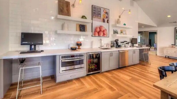 A modern kitchen with a built-in oven, a refrigerator, and a sink. There are stools and a dining table visible. - Lovely 2-Bdrm unit with pool. Home away from home. (Naperville)