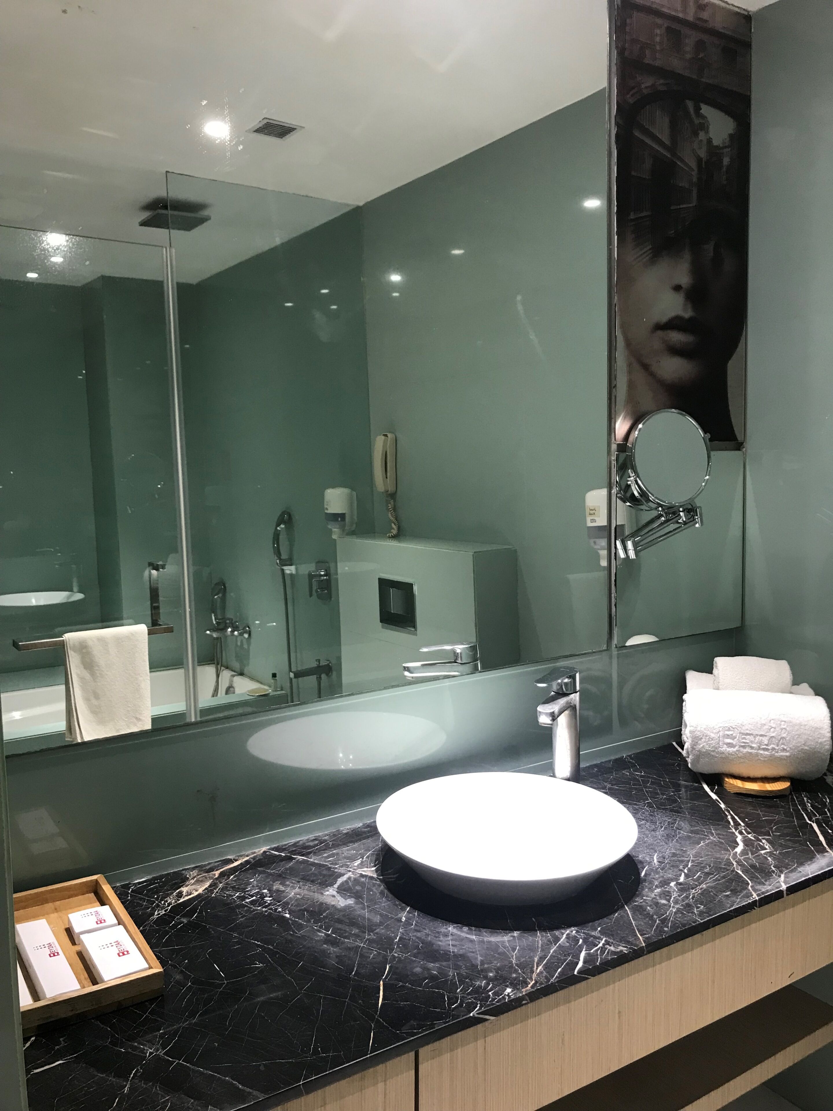A modern bathroom with a large mirror, a round sink, and a marble countertop.