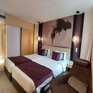 A hotel room with a large bed, two bedside tables, a brown armchair, and a wall-mounted artwork. - Beyzaa Hotel & Suites , Kolkata (Barasat)