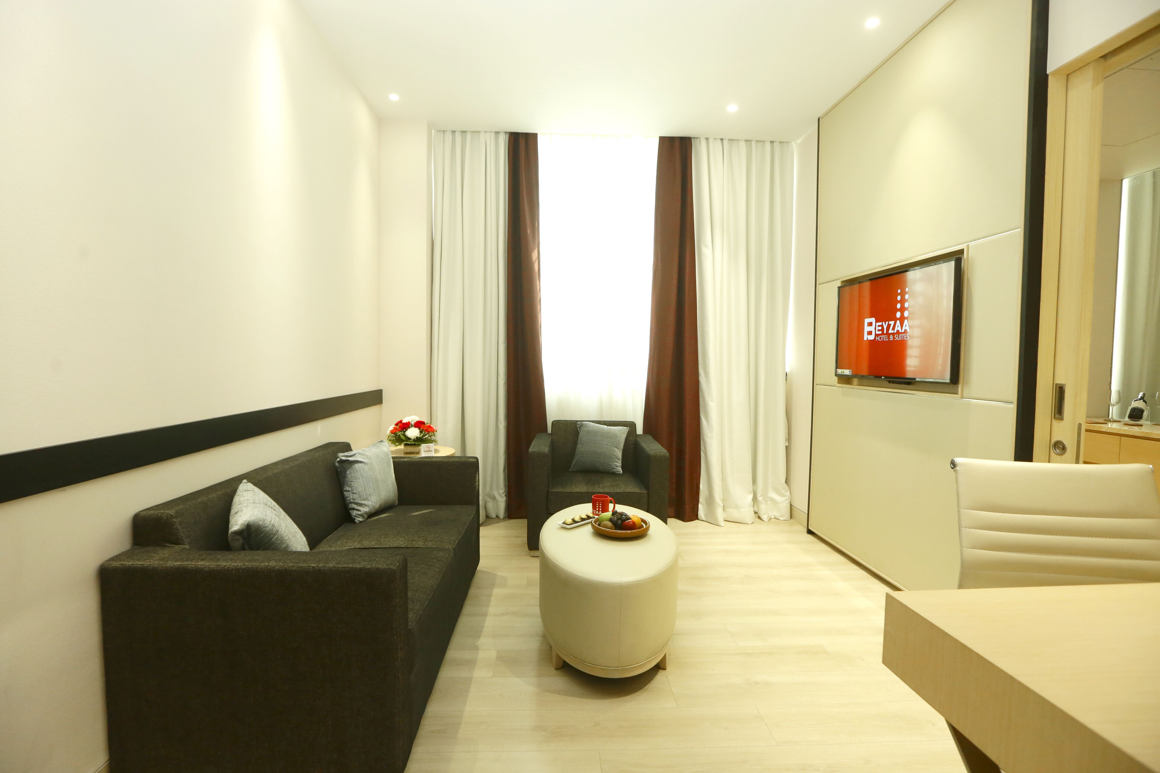 A modern hotel room with a sofa, ottoman, and a TV mounted on the wall.