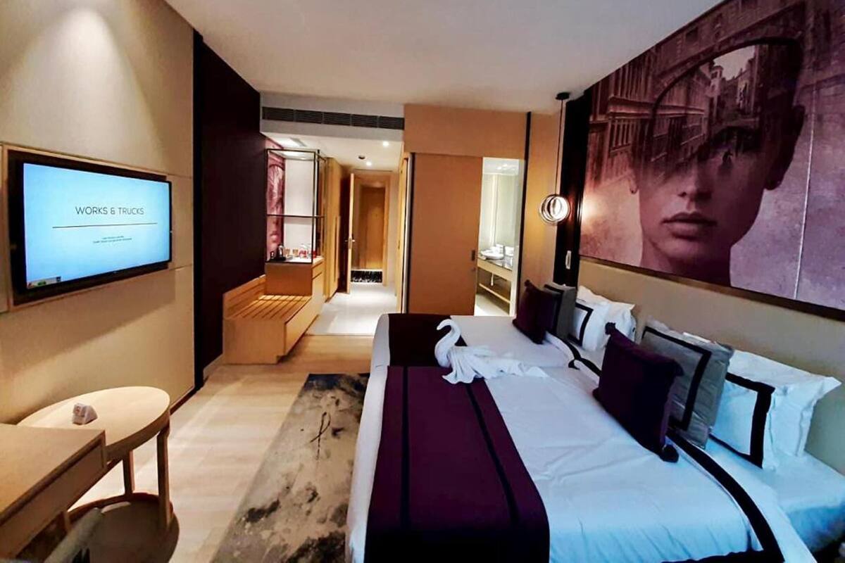 A hotel room with a bed, a TV, a desk, and a bathroom visible in the background.