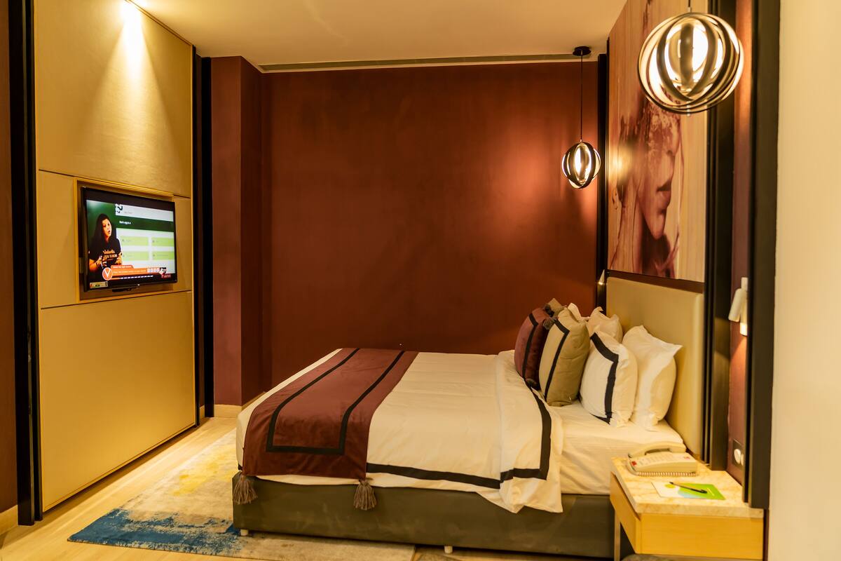 A hotel room with a bed, a television on the wall, and a nightstand with a phone and a notepad.