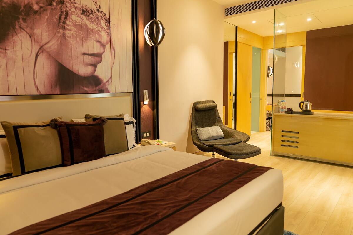 A hotel room with a bed, a chair, a desk, and a mirror.