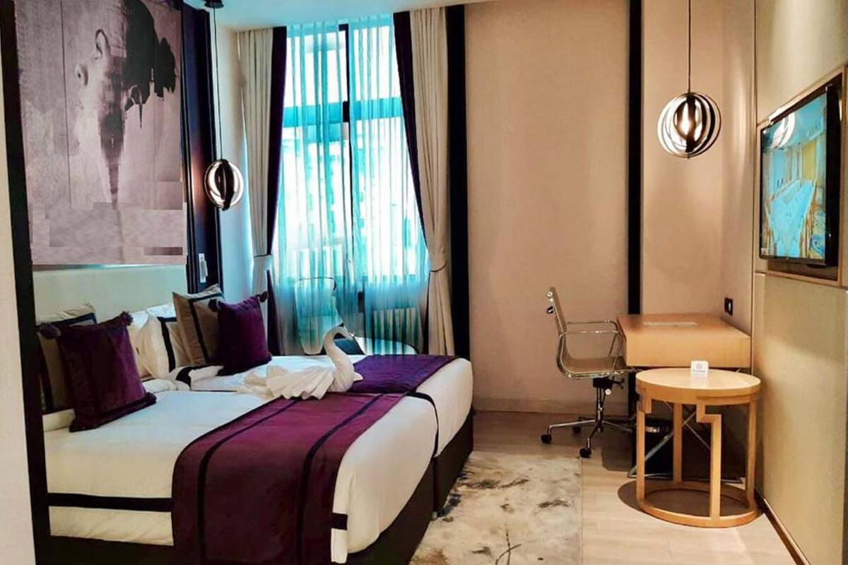 A hotel room with a bed, a desk, a chair, a round table, and a painting on the wall.