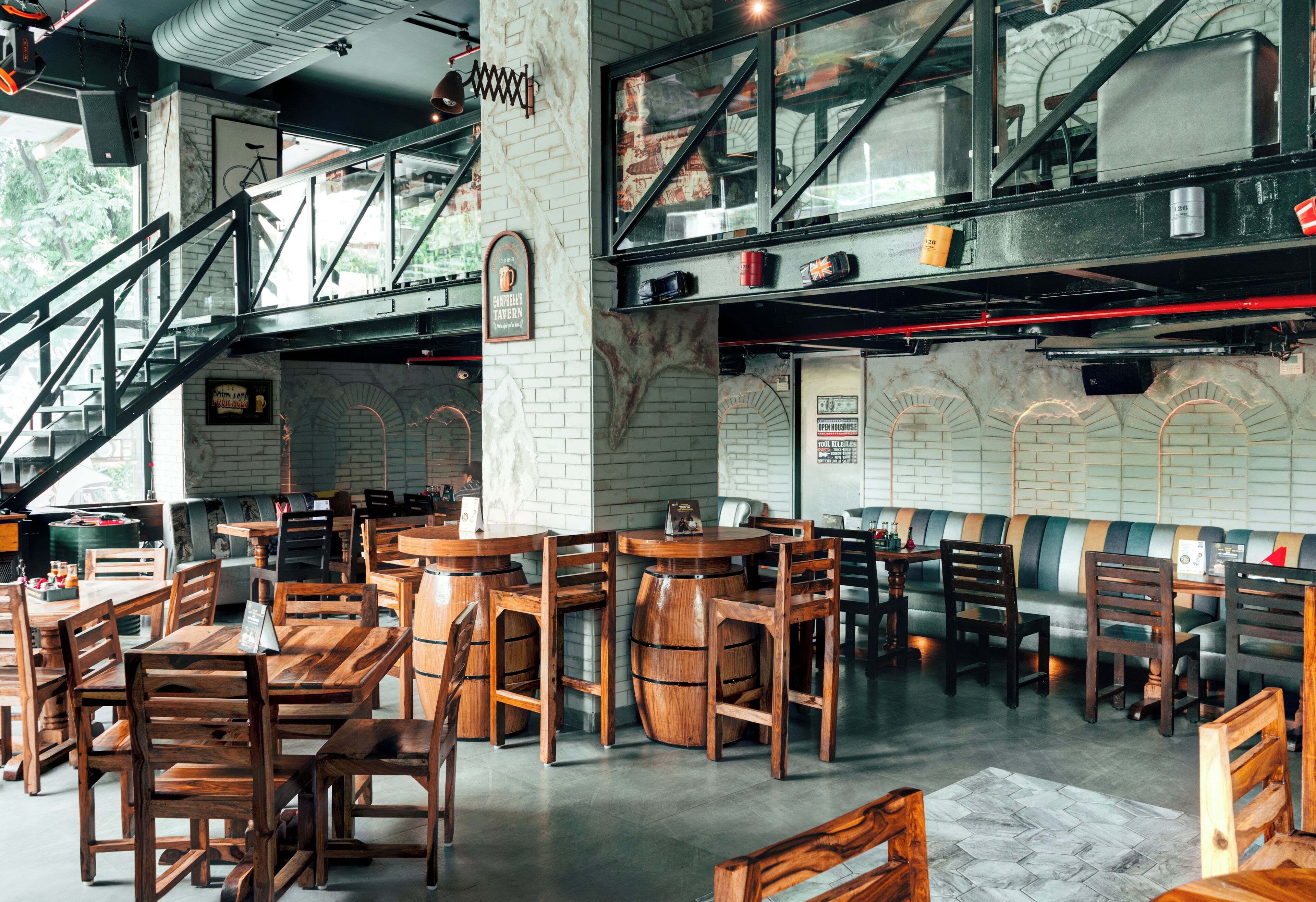 A restaurant with wooden tables and chairs, a staircase, and brick walls.