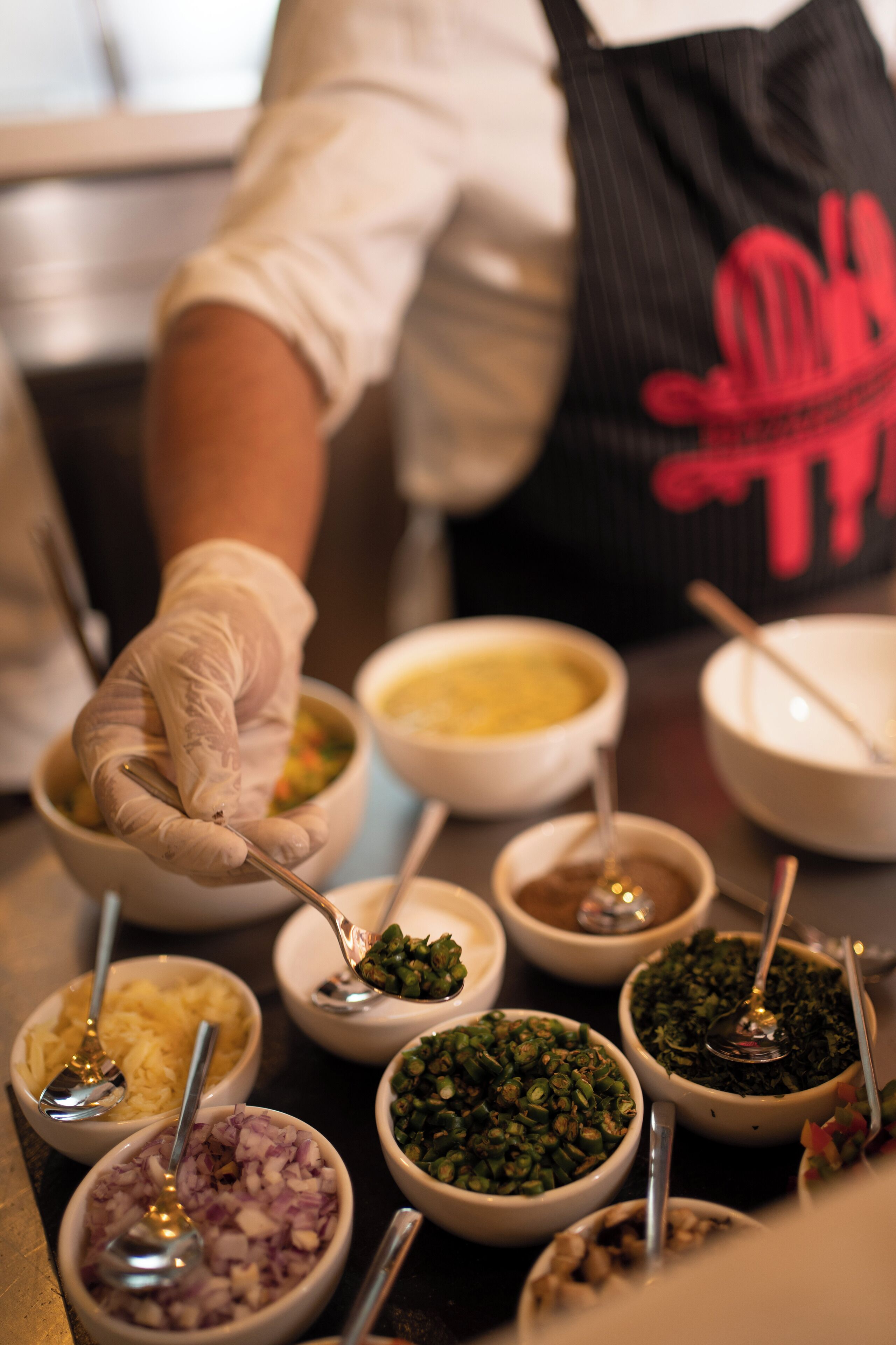 A person wearing a white shirt and black apron with red text, preparing food with various ingredients in bowls.