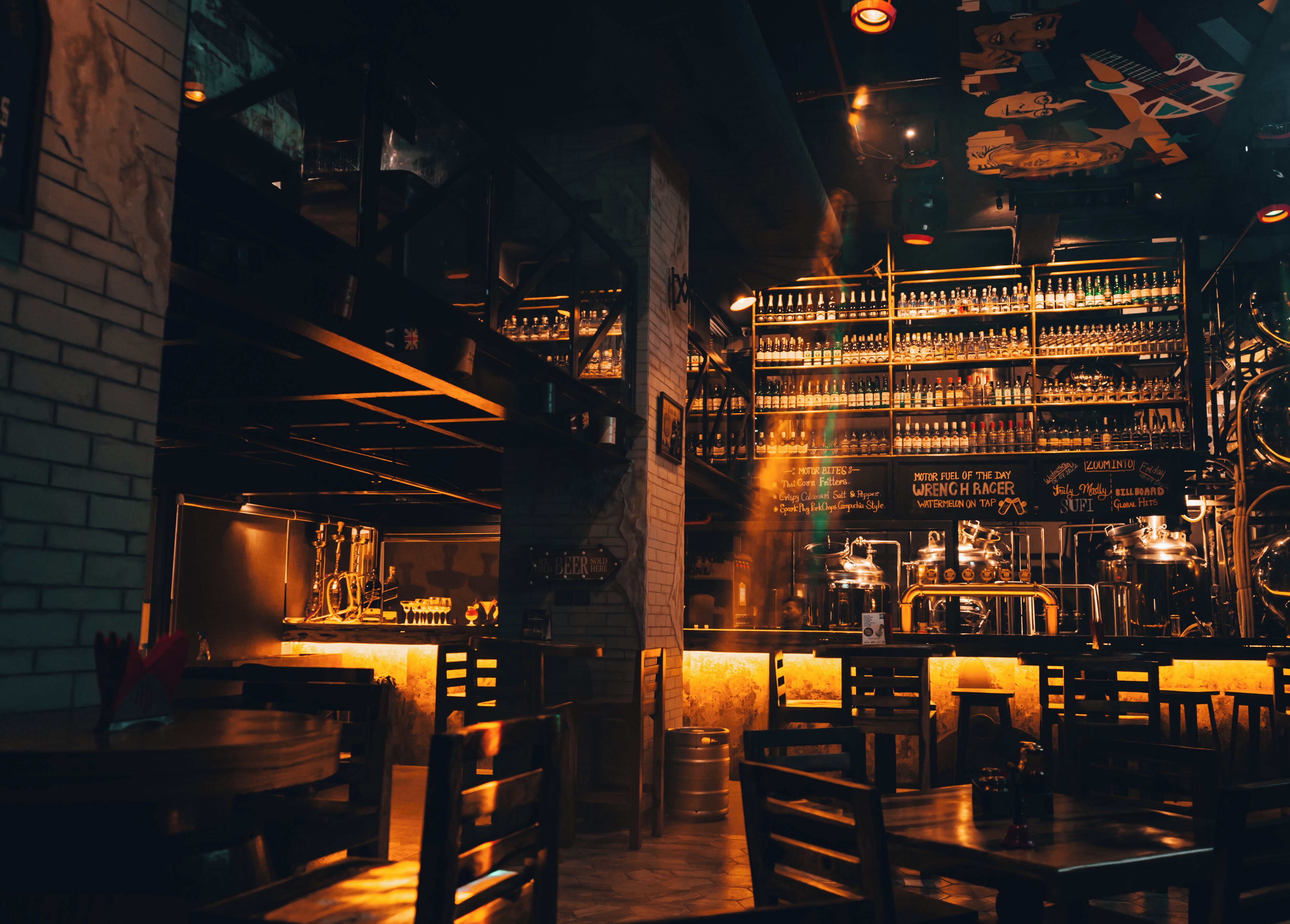 A dimly lit bar with wooden furniture and shelves stocked with bottles.