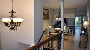 A spacious living area with a staircase, a dining area, and a kitchen with white cabinets and a large window.