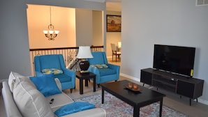 A living room with a sofa, two armchairs, a coffee table, a TV, and a lamp.