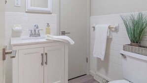Un bany amb un lavabo blanc, un mirall, un vàter i una planta en test.