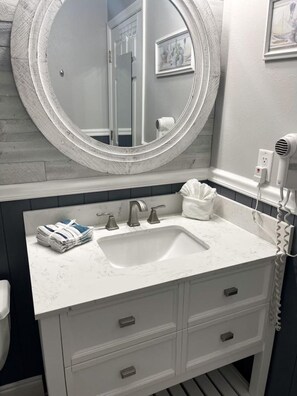 A bathroom with a white sink, two faucets, a round mirror, and a hairdryer on the wall.