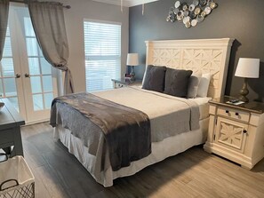 A bedroom with a large bed, two bedside tables, a nightstand, a wall clock, and a window with curtains.