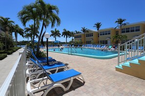 A pool area with lounge chairs, palm trees, and a building in the background.