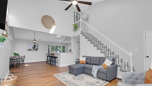 A spacious living area with a grey sectional sofa, a wooden floor, a staircase, and a kitchen in the background. - Spacious, 3 bedroom home, finished basement on quiet court (St. Peters)