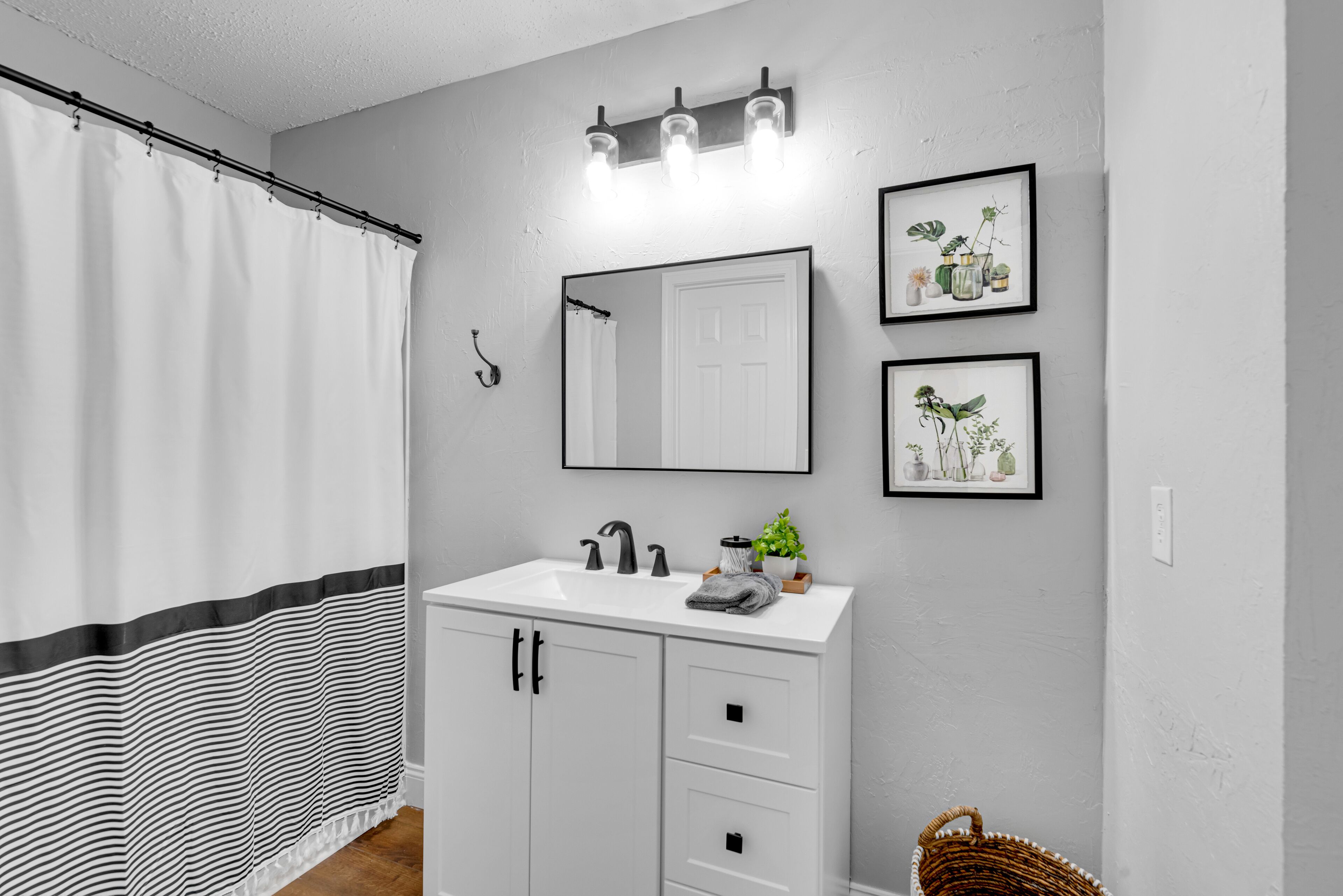 A bathroom with a white vanity, a mirror, and three framed botanical prints on the wall.
