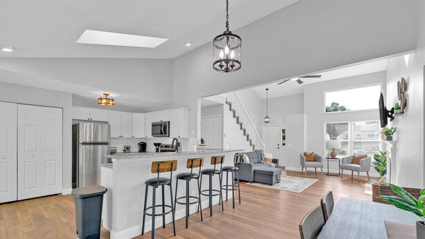 A spacious kitchen with white cabinets, a central island with bar stools, a stainless steel refrigerator, and a microwave. - Spacious, 3 bedroom home, finished basement on quiet court (St. Peters)