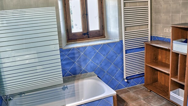 Un bagno con una vasca, una finestra con persiane in legno, un portasciugamani e una scaffalatura.
