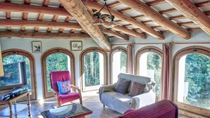 Un'ampia stanza con soffitto alto, travi in legno e ampie finestre ad arco che offrono vista sul verde circostante.