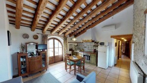 Una cocina rústica con vigas de madera, un comedor con mesa y sillas, y una sala de estar con sofá.