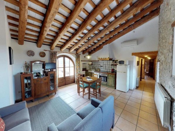 A rustic kitchen with wooden beams, a dining area with a table and chairs, and a living room with a sofa. - ELS CINGLES - Can Burgues (Santa Eulàlia de Ronçana)