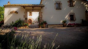 Un edificio tradicional con tejado de tejas, una entrada central con puerta de madera y plantas en macetas alrededor de la entrada.