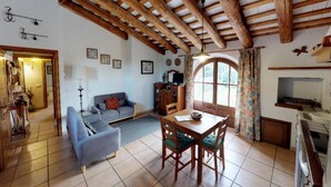 Una sala rústica con techo de madera, un sofá, una mesa de comedor con sillas y una zona de cocina con fregadero y armarios.