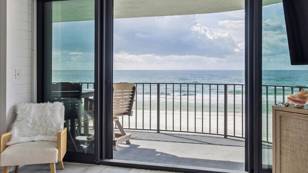 A balcony with a view of the ocean, a chair, and a table.