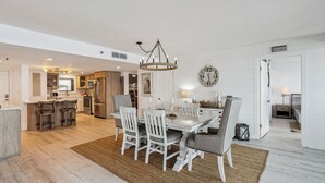 A spacious dining area with a large table and chairs, a chandelier, and a clock on the wall.