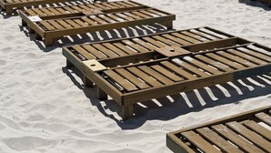 A beach with wooden lounge chairs and blue umbrellas.