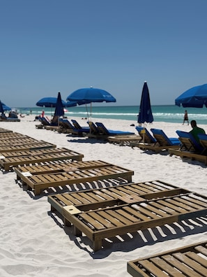 A beach with wooden lounge chairs and blue umbrellas.