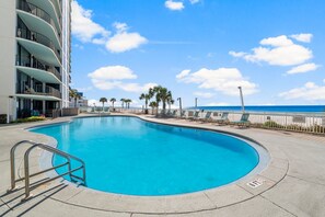 A swimming pool with a curved edge, a metal handrail, and a view of the ocean.