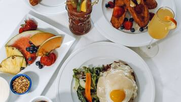 A breakfast spread with various dishes including toast, fruit, a salad with an egg, and a drink.