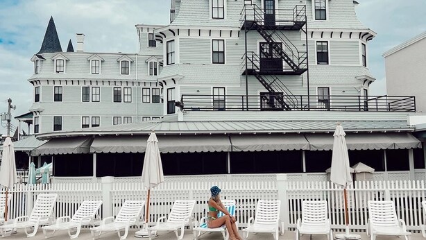 A poolside area with white lounge chairs and a person sitting on one. - The Inn of Cape May (Cape May)