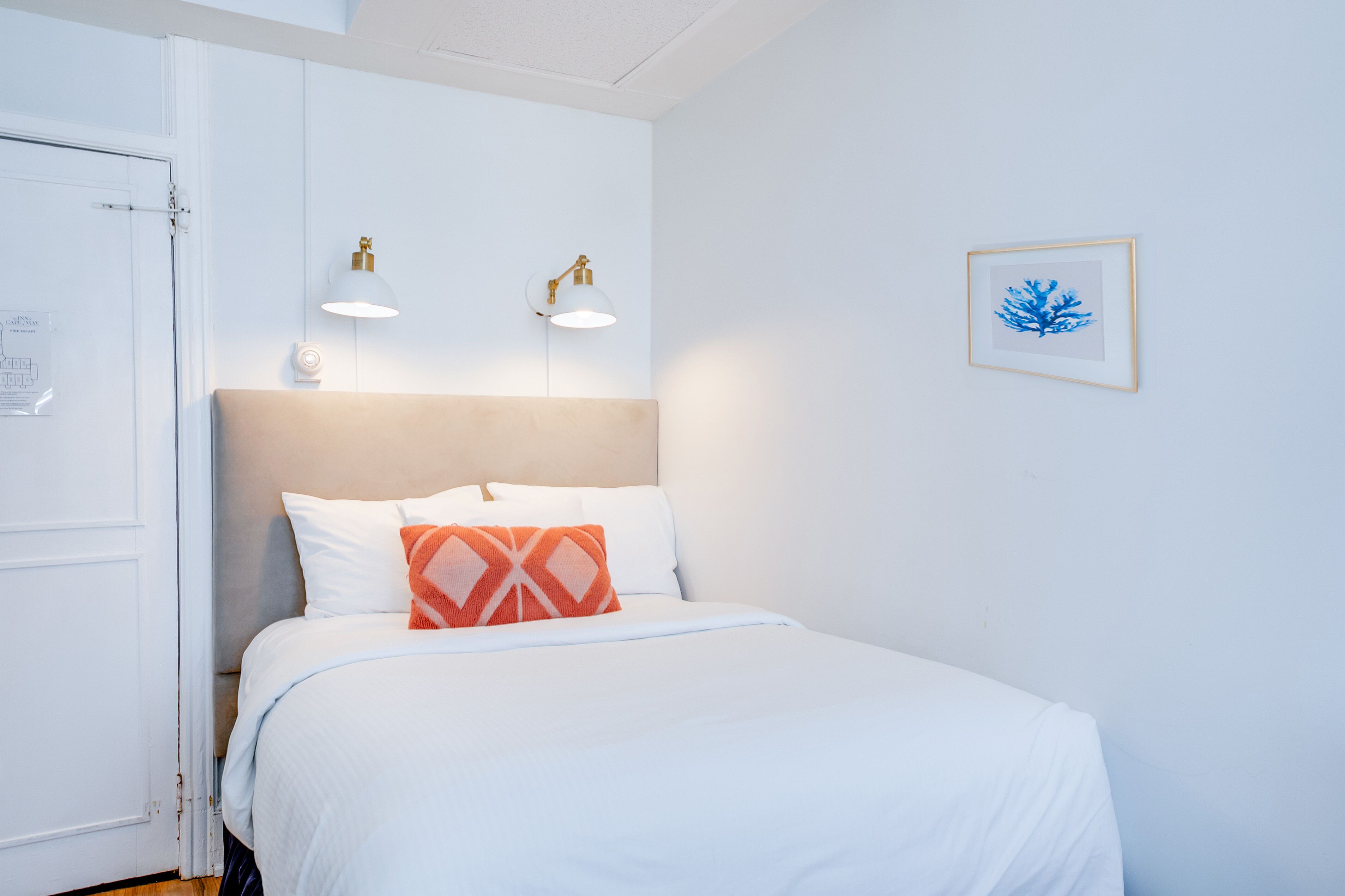 Una camera d'albergo con un letto, due luci a parete, un quadro incorniciato e una porta.