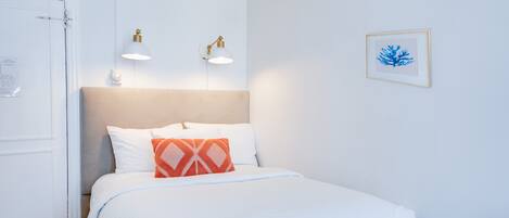 Una camera d'albergo con un letto, due luci a parete, un quadro incorniciato e una porta.