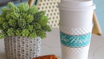 A croissant on a plate, a cup with a label, and a small potted plant on a table.