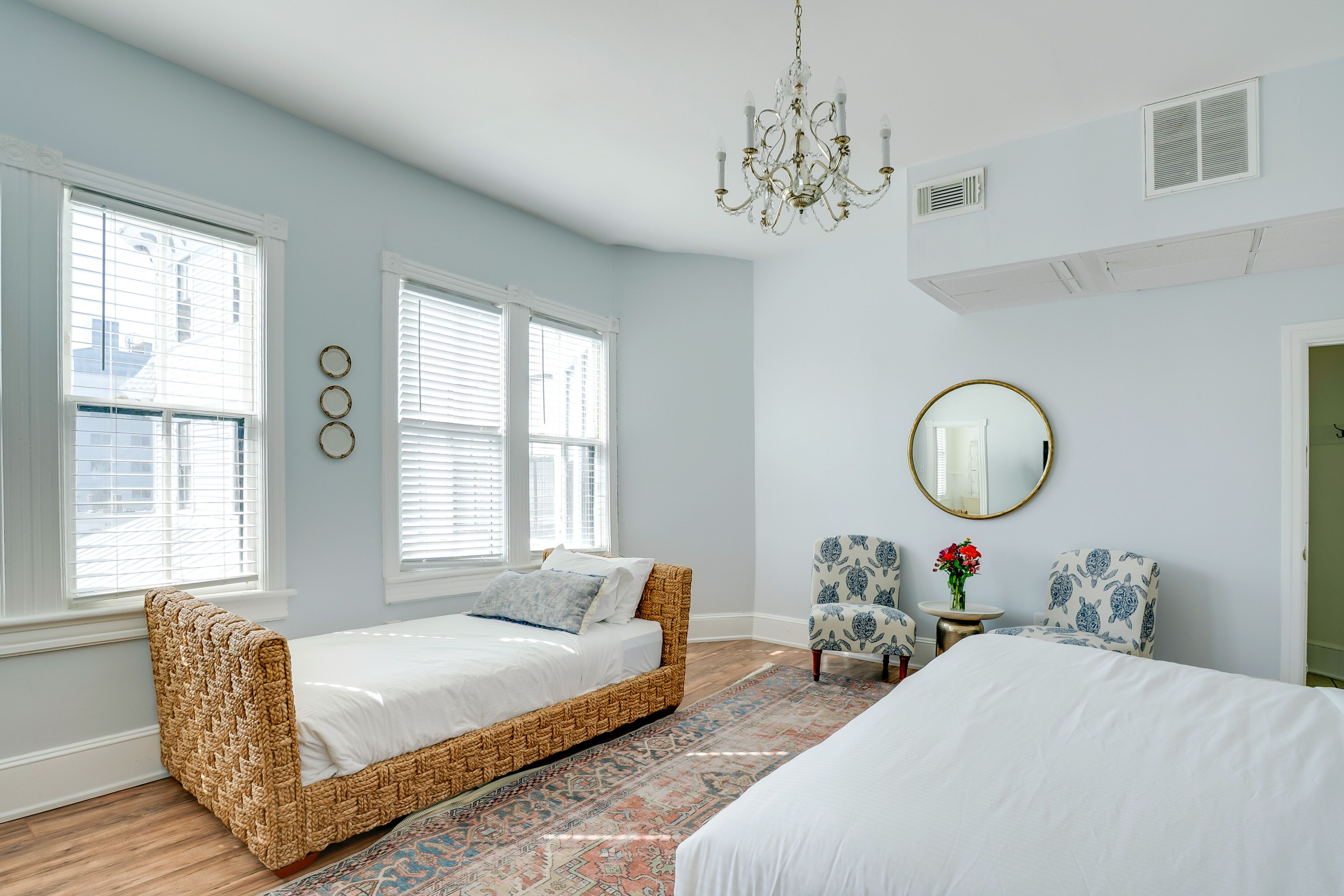 A bedroom with a bed, a daybed, two chairs, a mirror, and a chandelier.