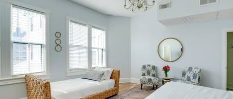 A bedroom with a bed, a daybed, two chairs, a mirror, and a chandelier.