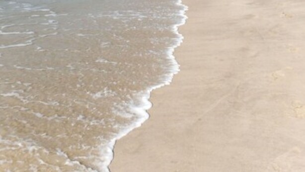 Ein Strand mit weitem, sandigen Ufer und sanften Wellen.